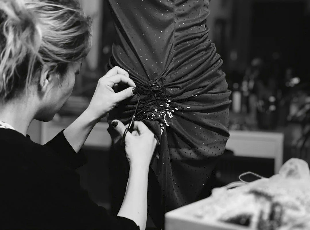 A woman sewing or altering a dark, polka-dotted dress with a laced-up detail.