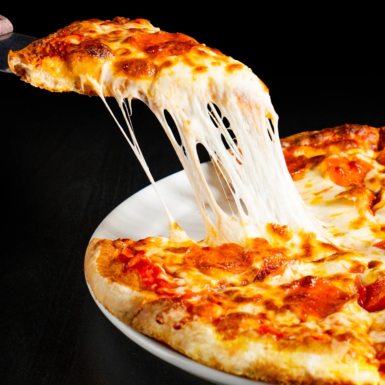 A slice of cheese pizza being lifted from a pizza pie, with melted cheese stretching.