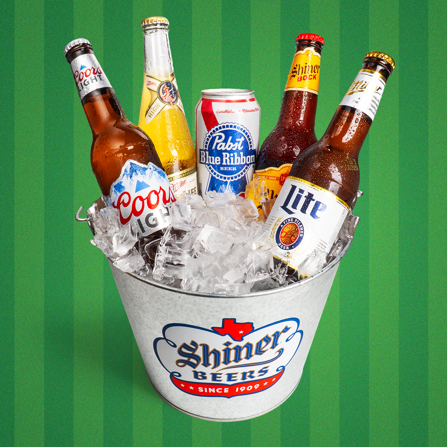 A metal bucket filled with ice and assorted beer bottles and a can, including brands like Coors Light, Miller High Life, Pabst Blue Ribbon, Shiner Bock, and Miller Lite, with a green football field background.