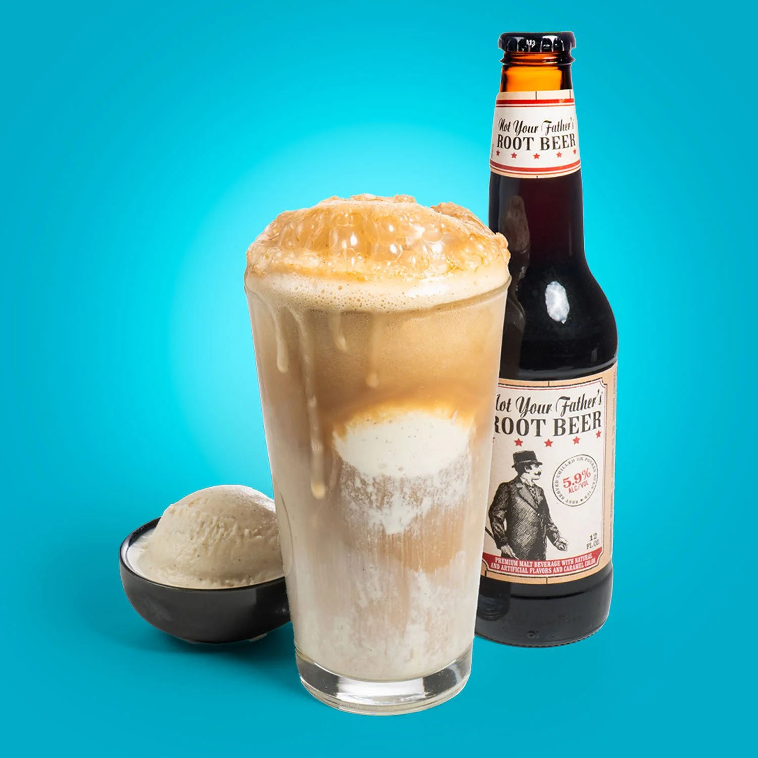 A root beer float in a tall glass with ice cream and frothy root beer, a scoop of vanilla ice cream in a black bowl, and a bottle of root beer in the background against a blue backdrop.