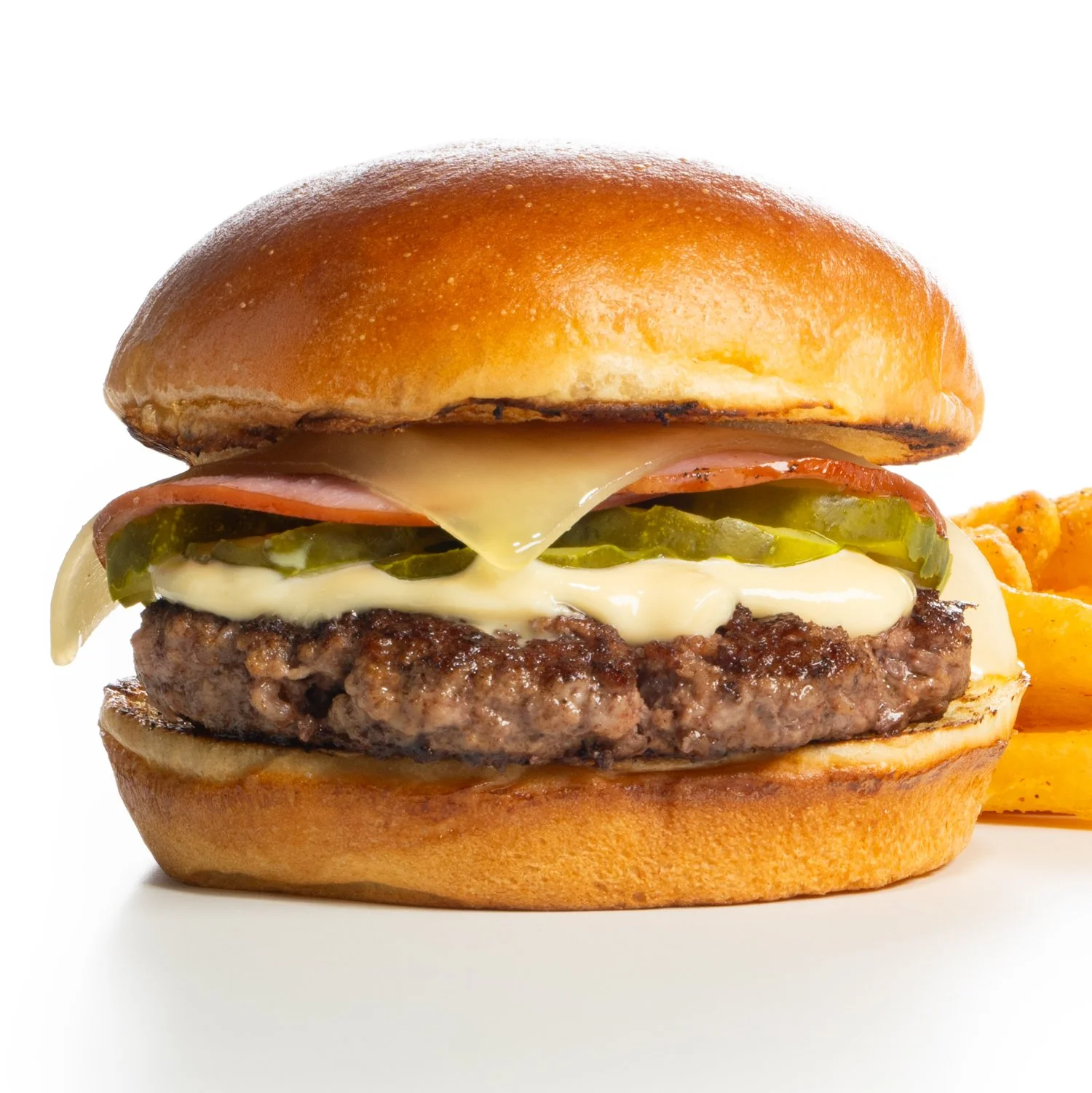 Close-up of a Cuban cheeseburger with a beef patty, melted cheese, pickles, ham, and a toasted bun, with a side of fries.