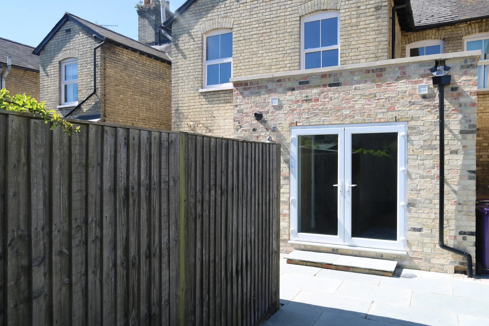 Backyard with a wooden fence, brick house with white-framed windows and glass door, and patio area with paving stones.