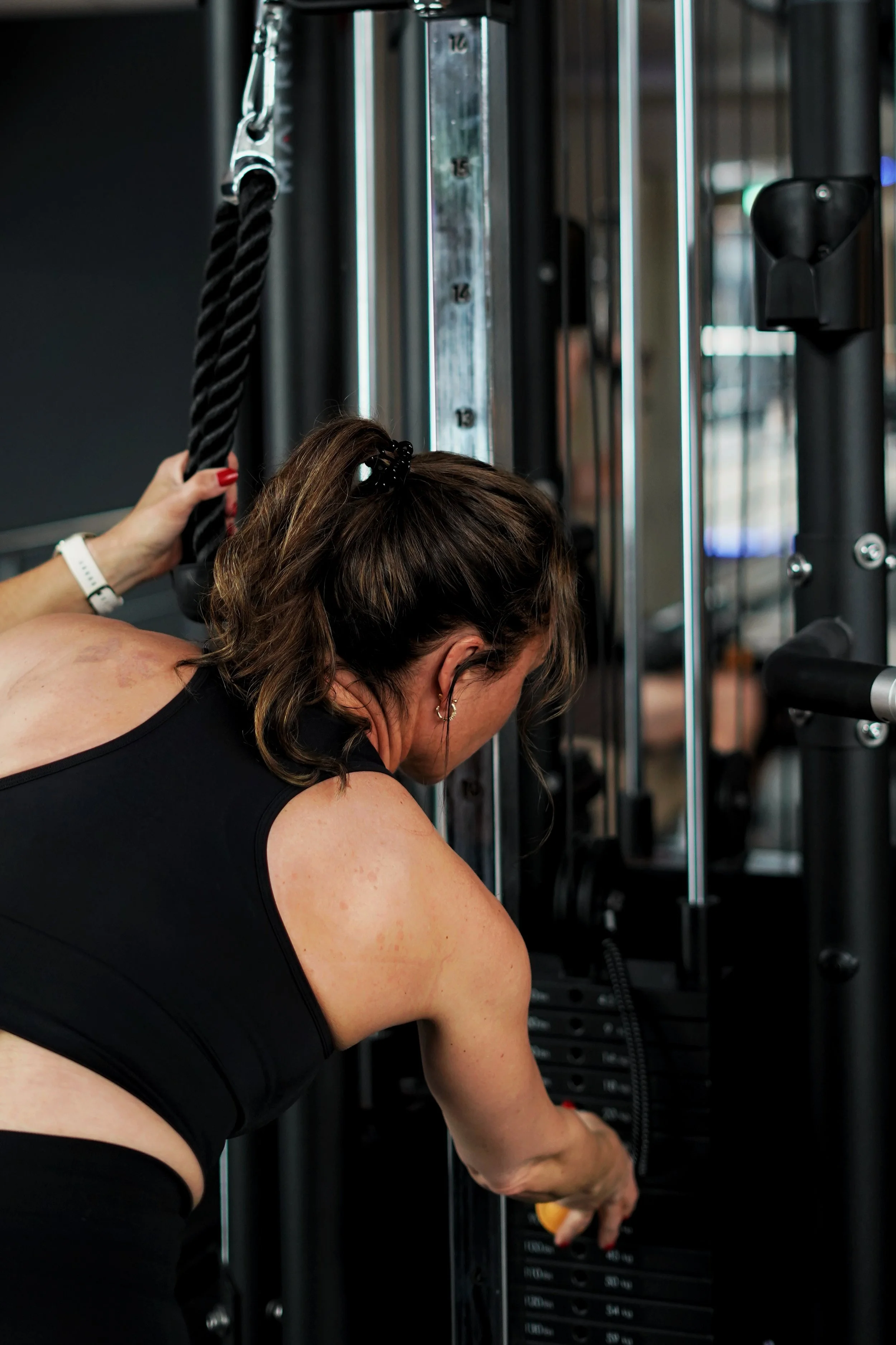 Vrouw die een gewichthefapparaat bedient in een sportschool, met focus op haar armen en schouders.
