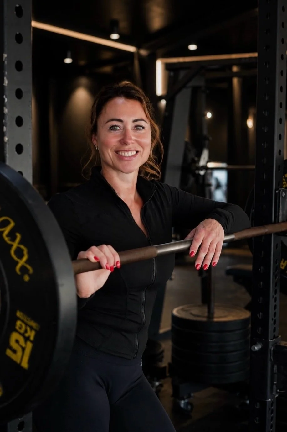 Een glimlachende vrouw in sportkleding die een halter heft in een sportschool.