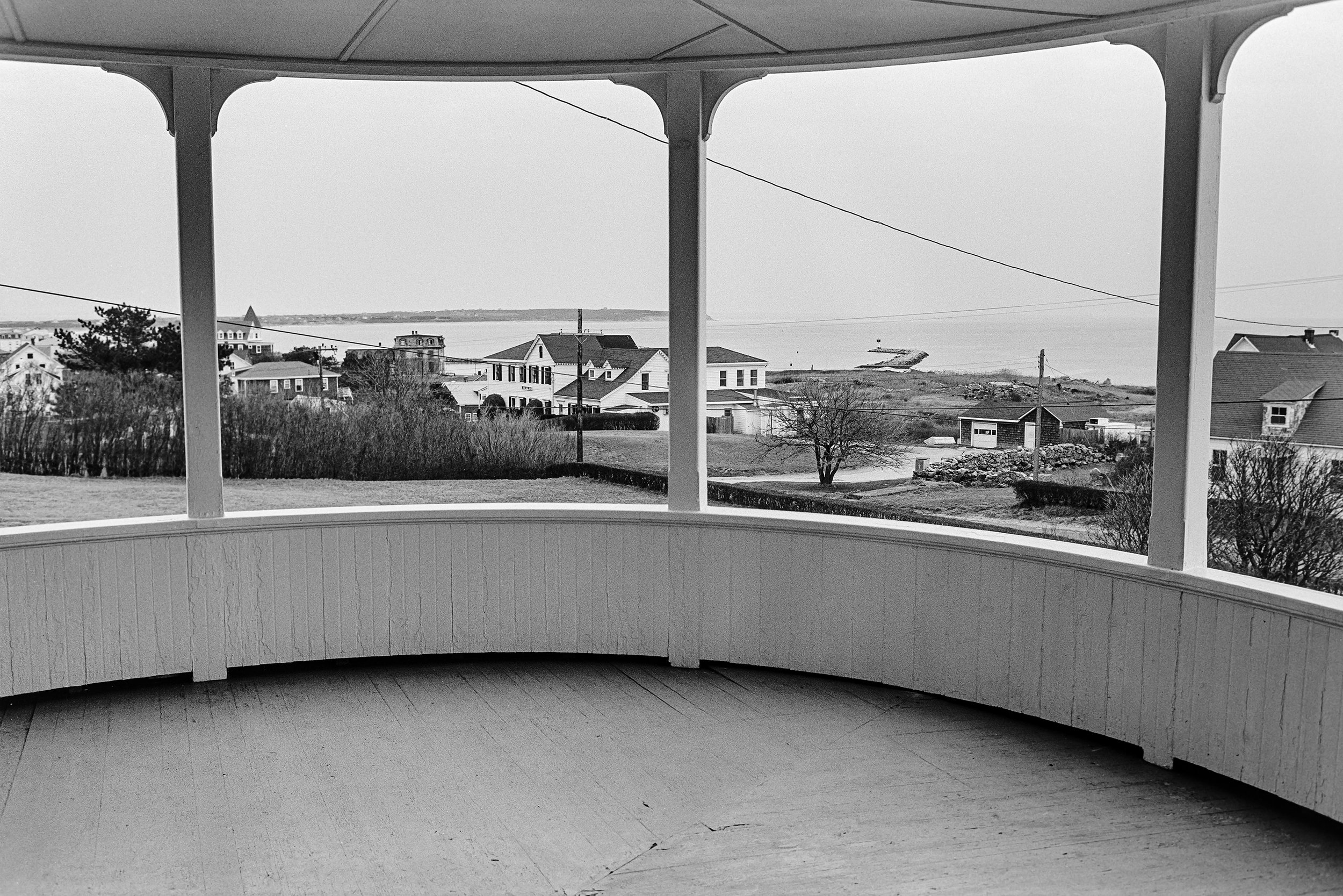 View from a porch with a painted railing, looking out over a yard with trees, houses, and a distant shoreline with water and land.