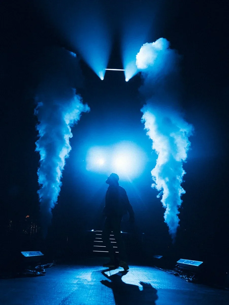 A singer silhouetted on stage with bright blue lights and smoke, creating a dramatic atmosphere.