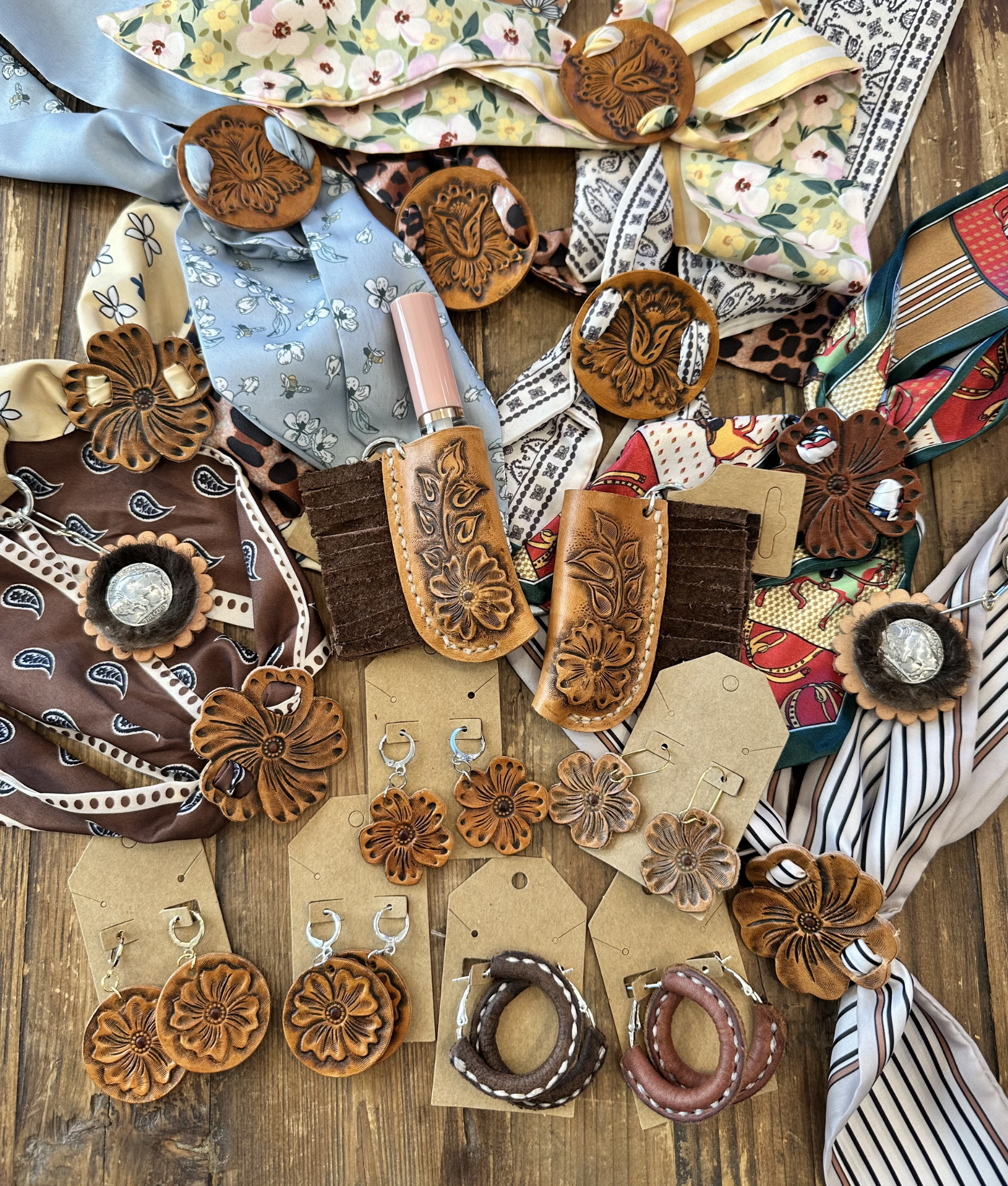 Various leather accessories, including belts, hairbands, and decorative pieces, displayed on a wooden surface. The items feature floral and intricate designs, some with engraved patterns and metal embellishments, with a mix of earthy tones and bright colors.