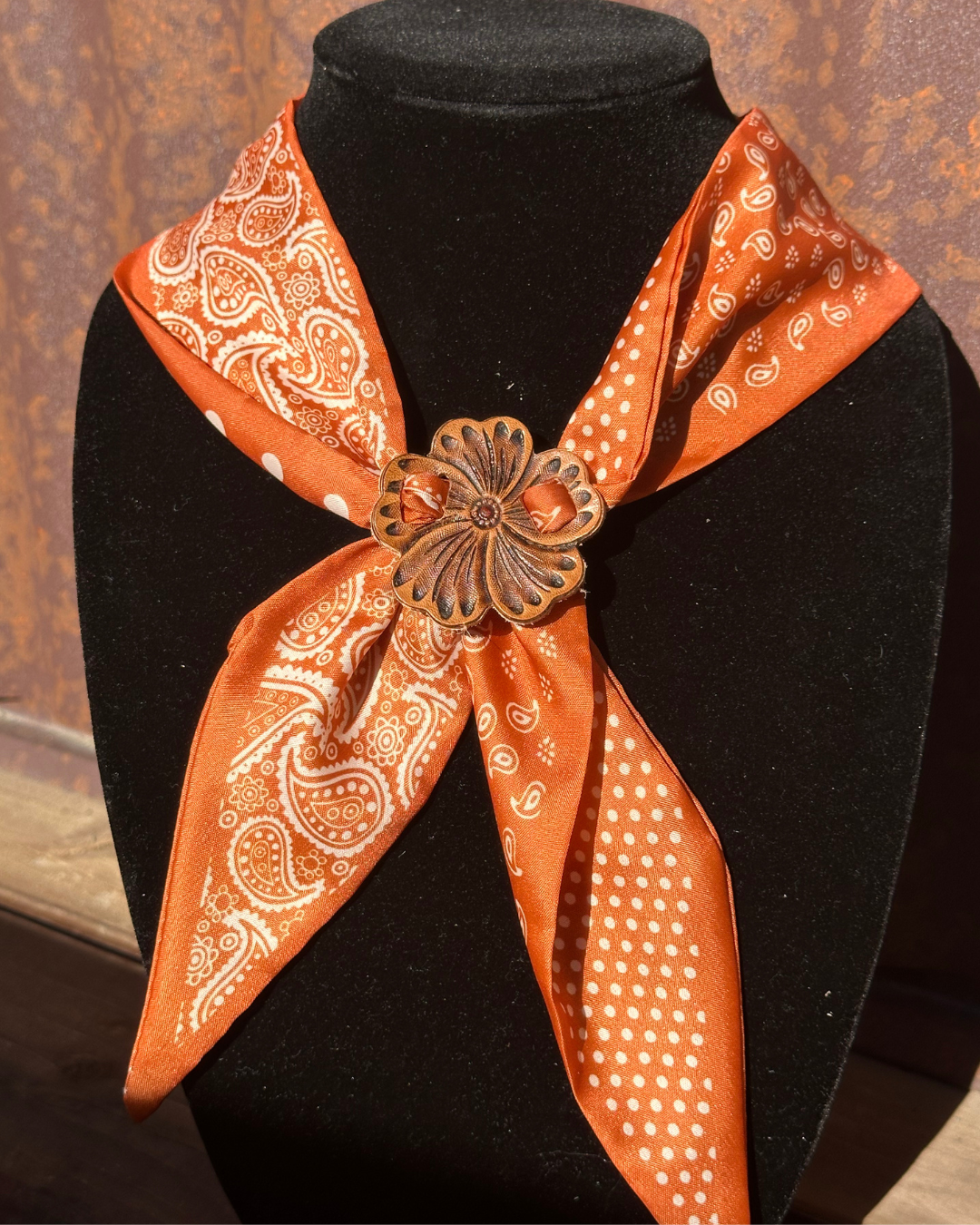 A black display bustwear with a large orange bandana featuring white paisley and polka dot patterns, tied in a knot at the front with a decorative flower-shaped metal brooch.