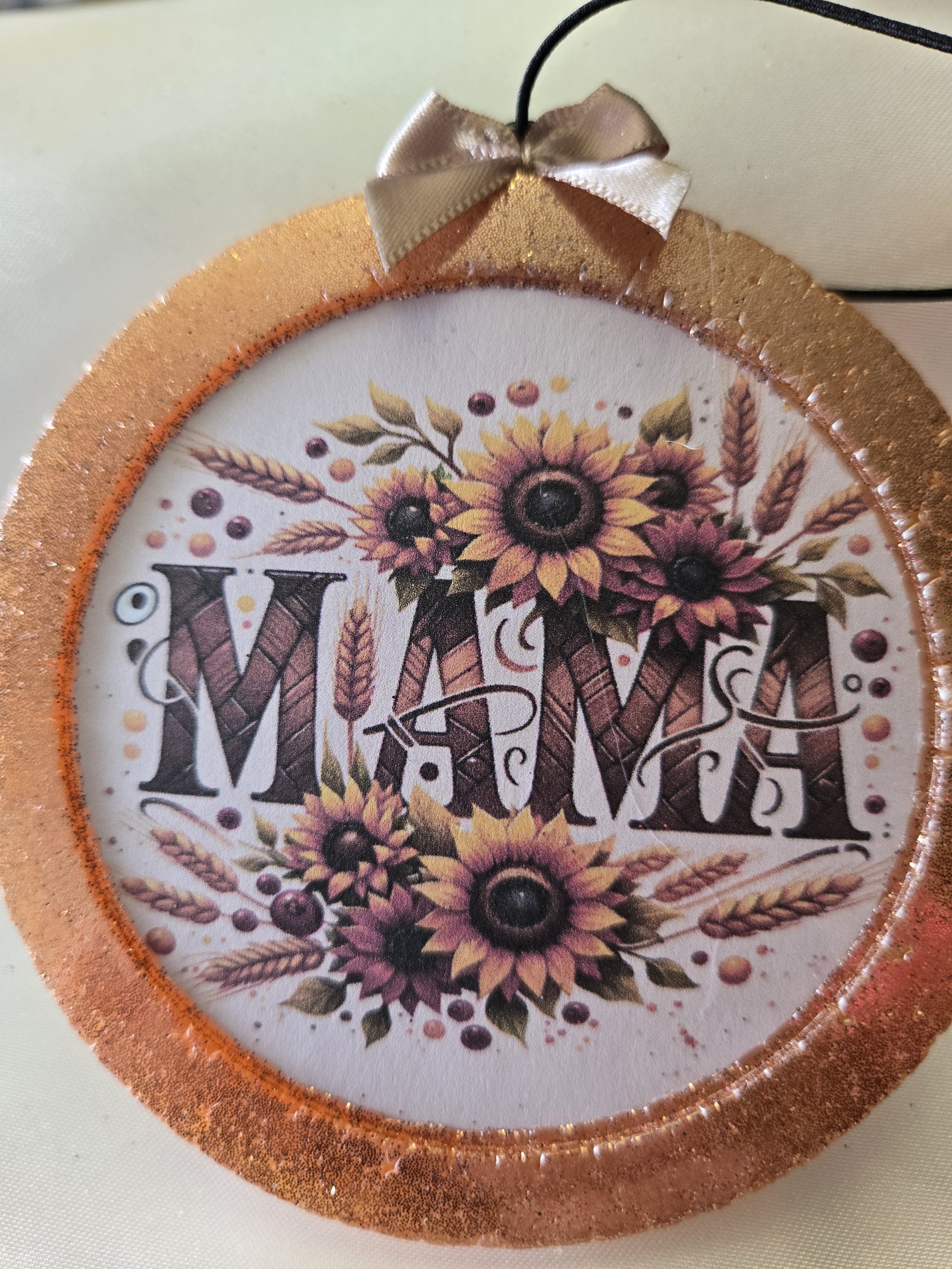 Close-up of circular decoration with sunflowers, wheat, and berries, surrounded by a glittery orange border, and a small beige bow at the top.