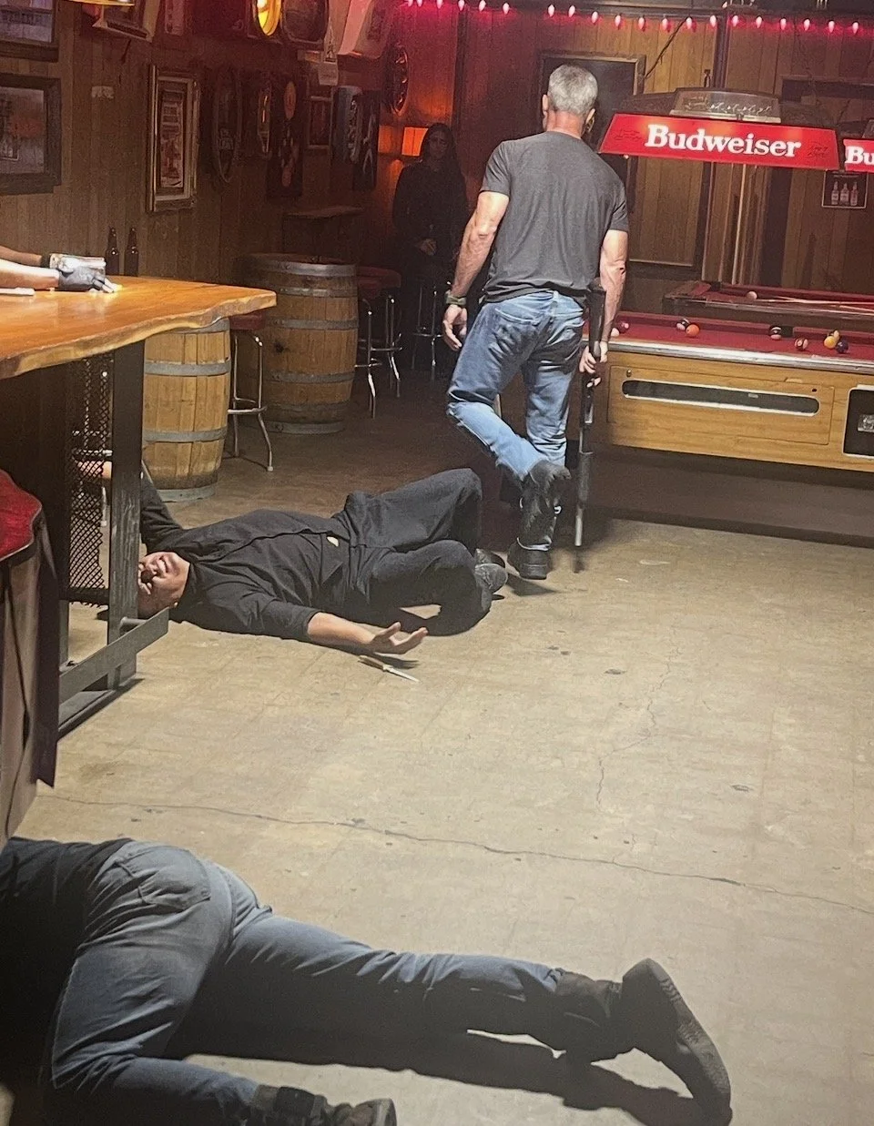 A person lying on the floor of a bar, with two others nearby, one standing next to a pool table.