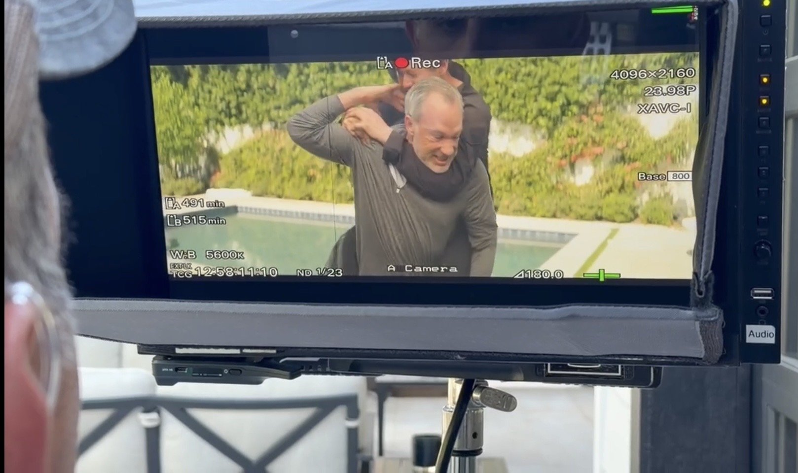 Behind-the-scenes view of a film or video shoot showing a man laughing and Playfully pulling on his neck, captured on a camera monitor.