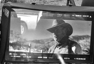 A person wearing a cowboy hat in front of a vehicle, captured on a camera screen.