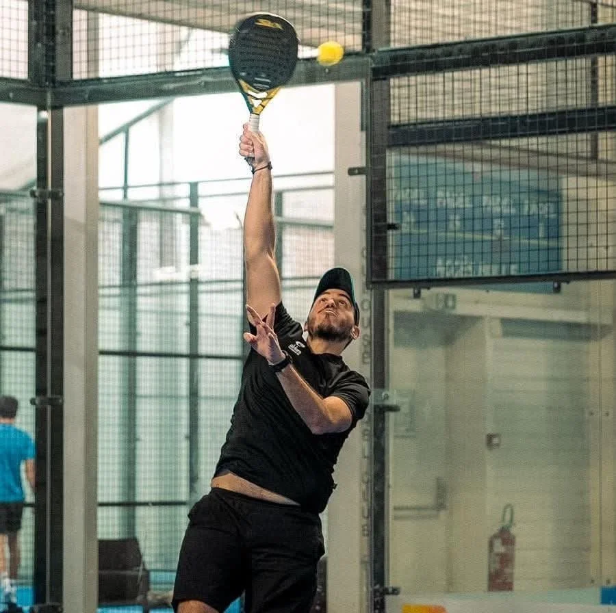 Homme jouant au tennis en salle, prêt à frapper une balle avec une raquette.