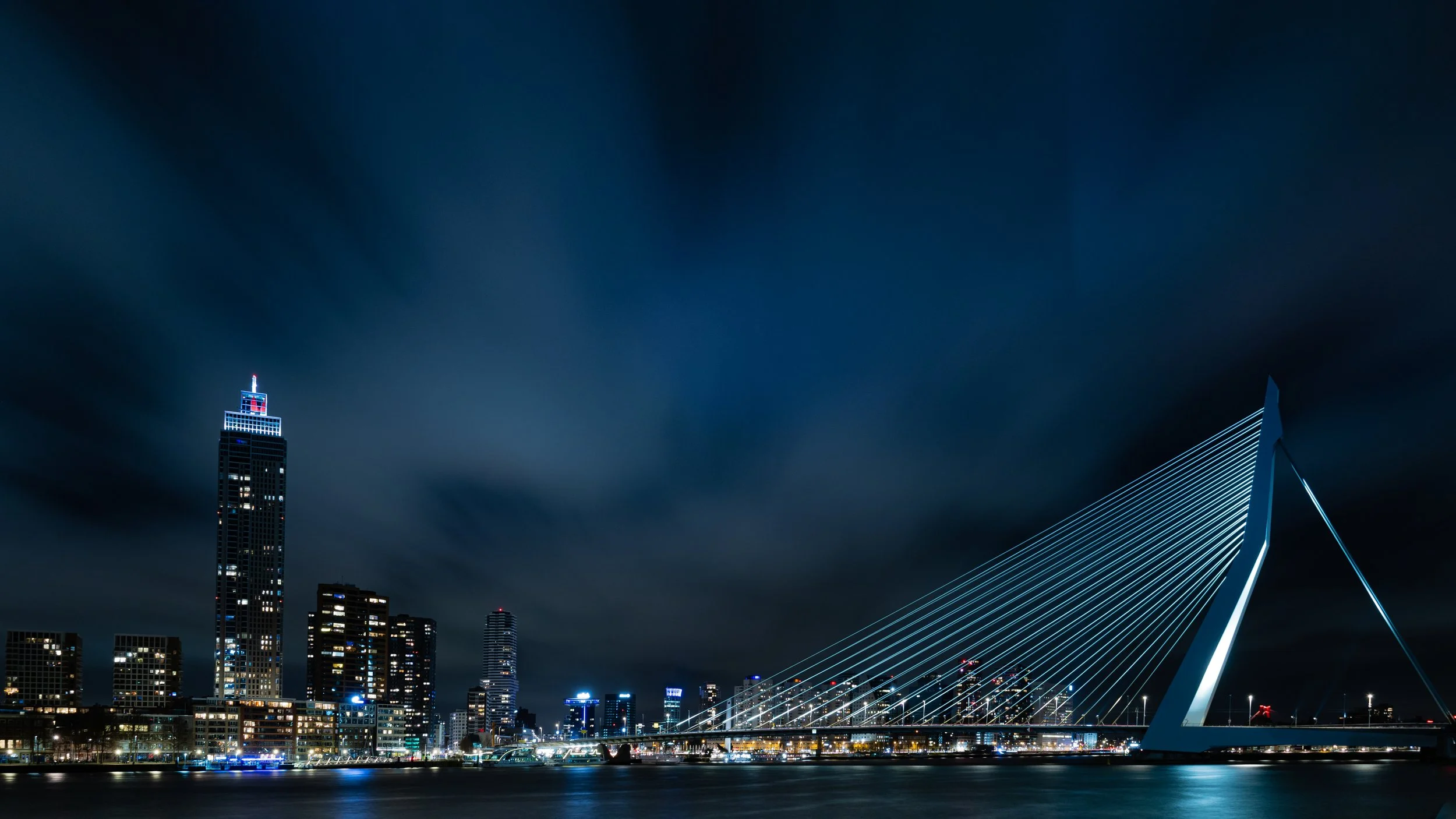 Erasmus Bridge and Rotterdam skyline at night with city lights reflecting on water — Netherlands — by ROEL | WILLEM