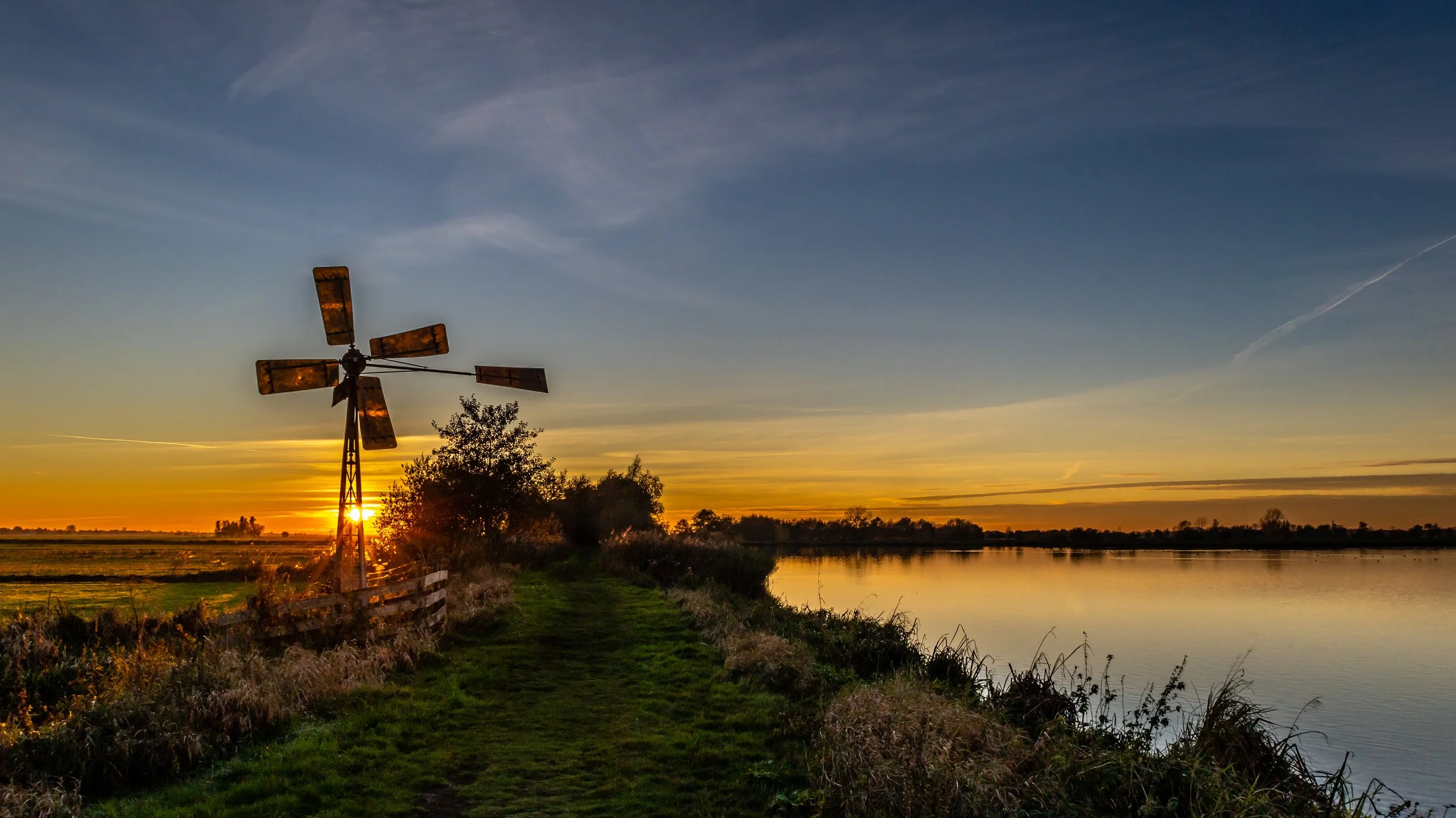 Dutch windmill at sunset beside calm water and a grassy path — Blokland, Montfoort — Netherlands — by ROEL | WILLEM