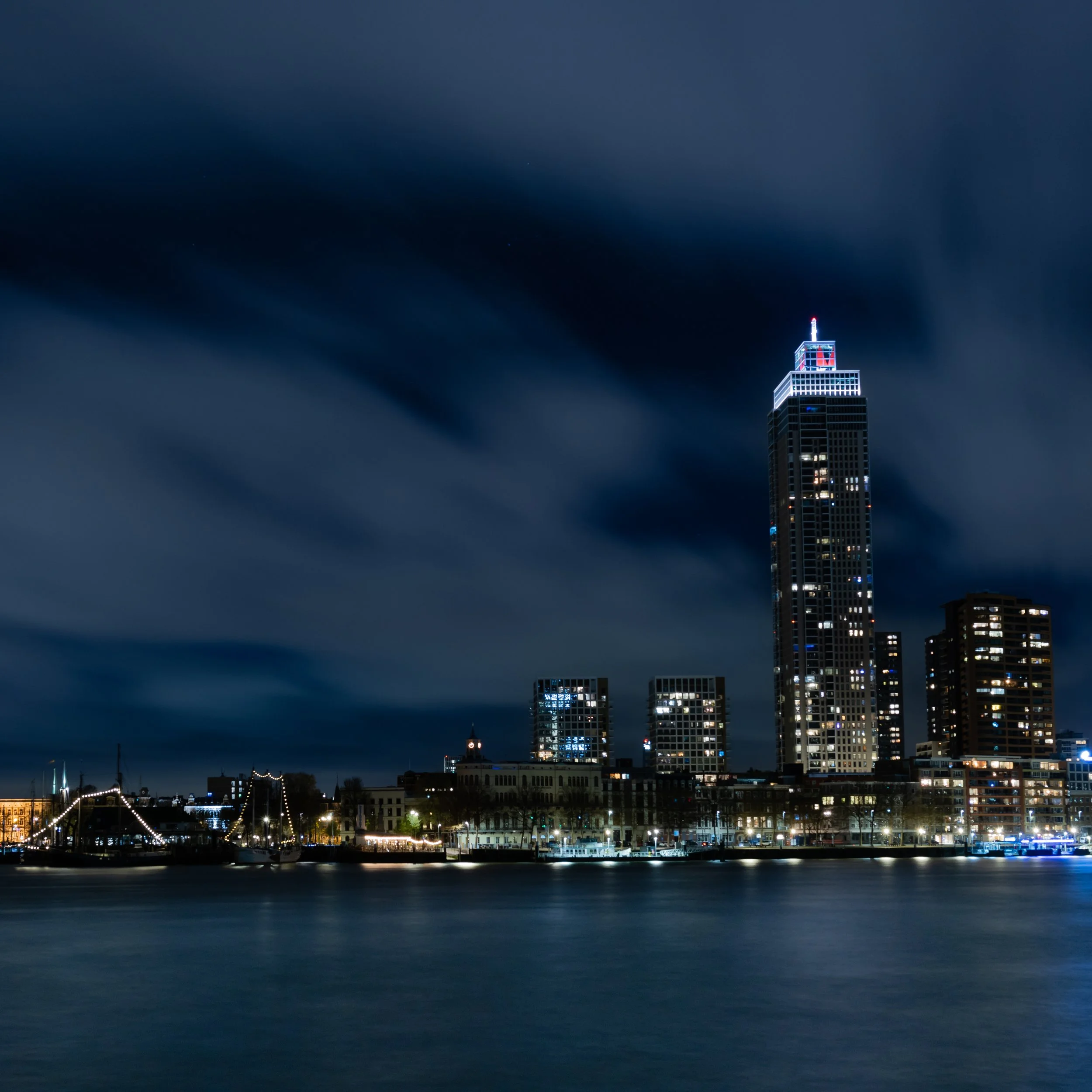 Rotterdam skyline at night with illuminated high-rise buildings and moving clouds — Netherlands — by ROEL | WILLEM