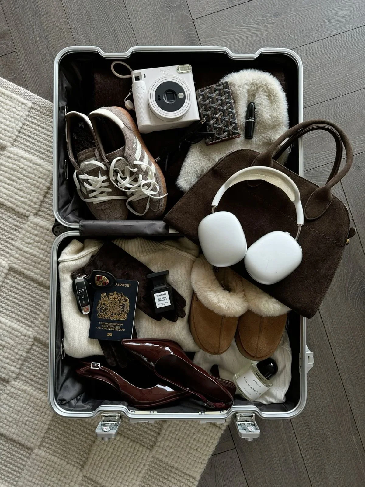 Open suitcase containing travel essentials including shoes, a camera, a wallet, headphones, a passport, gloves, a key fob, a bottle, and various clothing items.