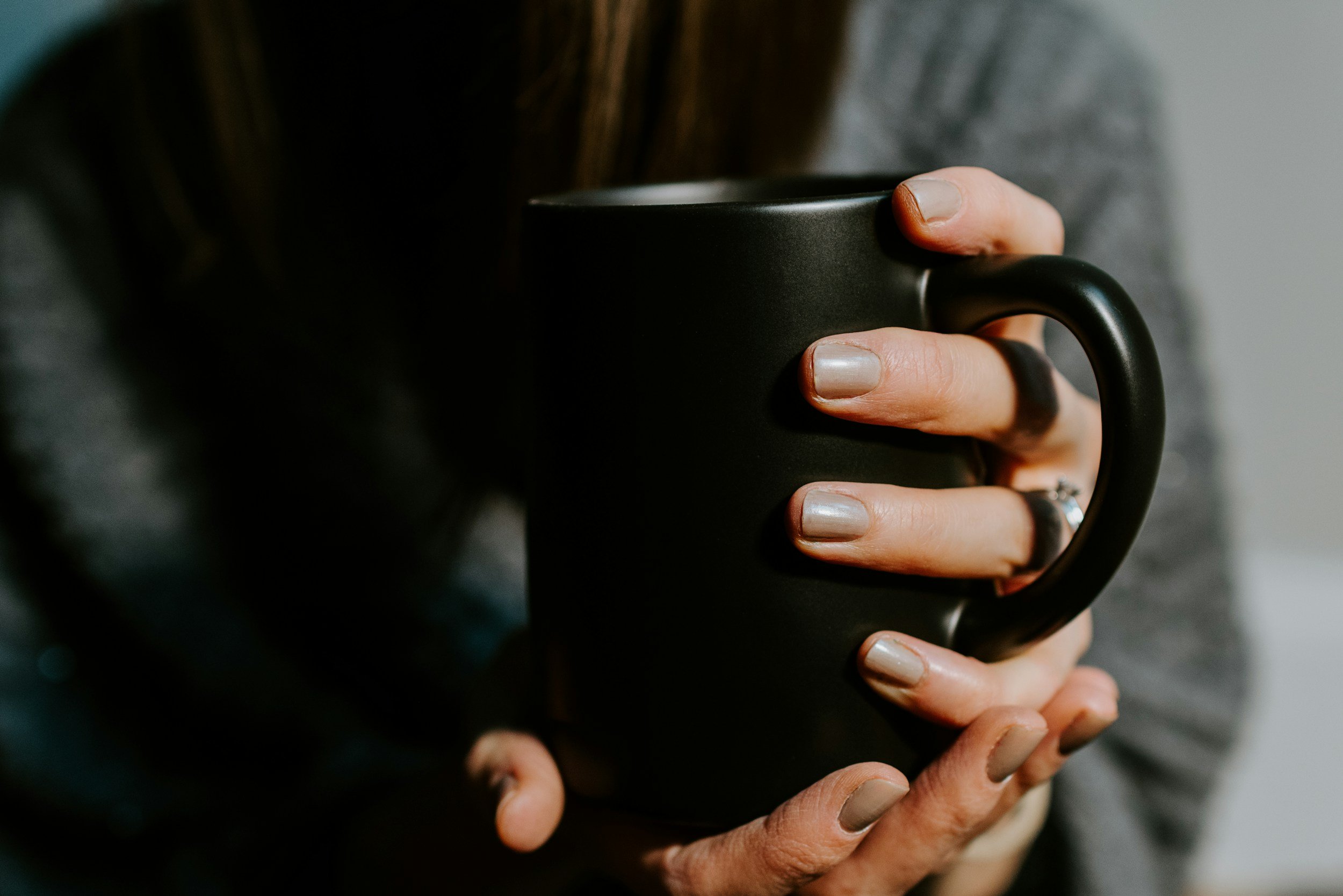 A person's hand holding a black ceramic mug.