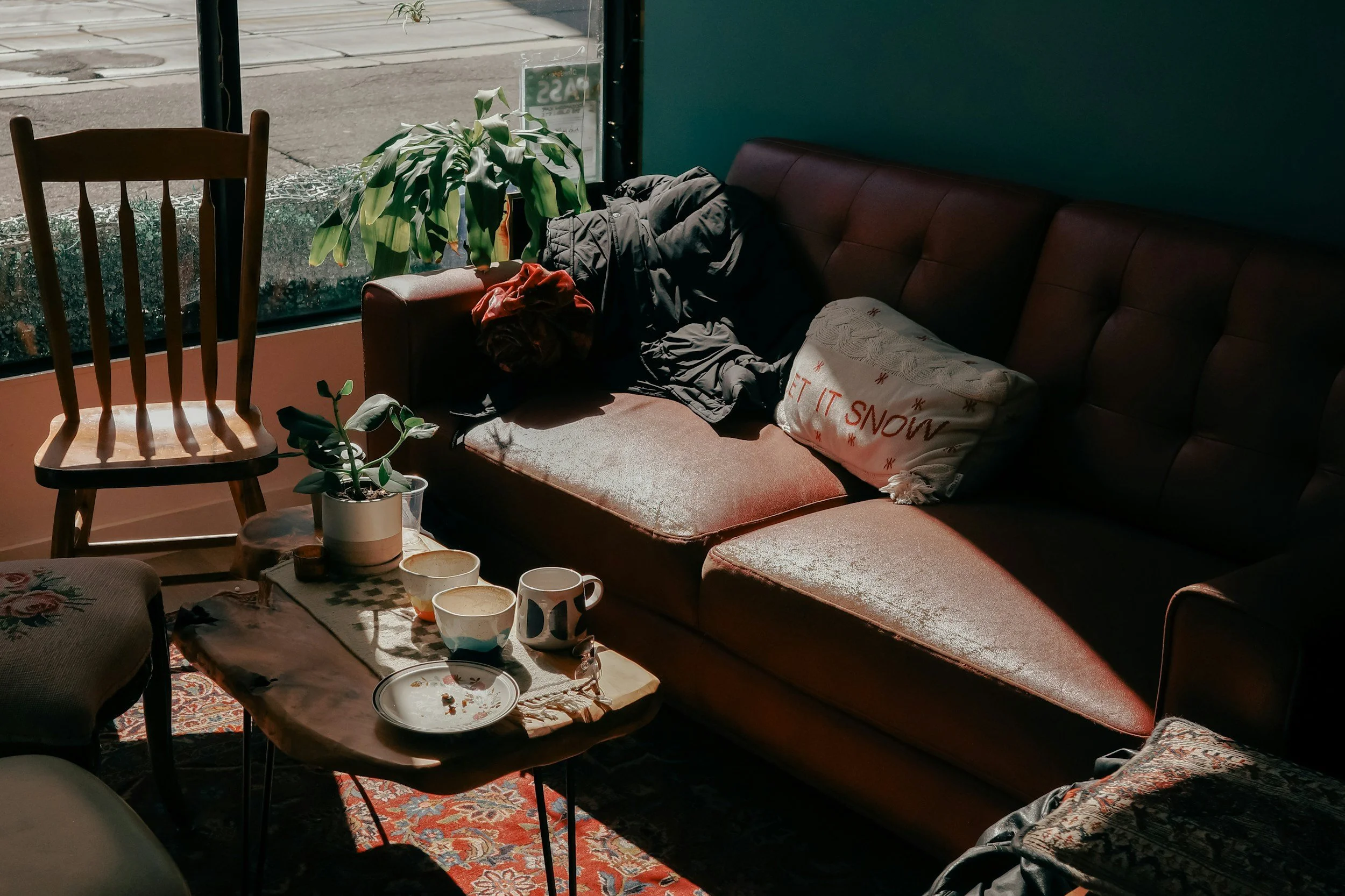 Inside a cozy cafe with a brown couch near a large window. The couch has a jacket and a pillow with