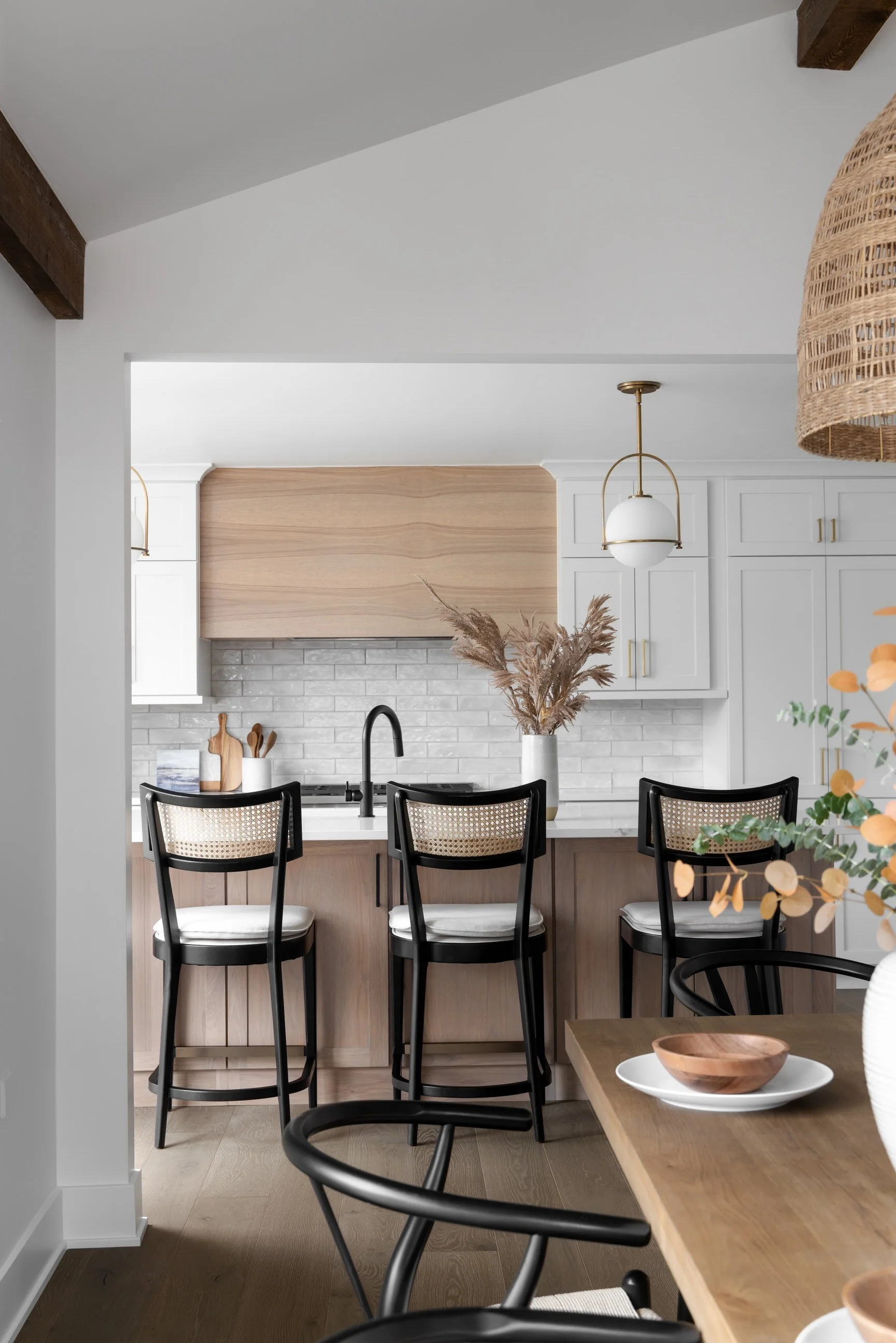 Kitchen island with dark black stools against white cabinetry paired back to warm wood tones