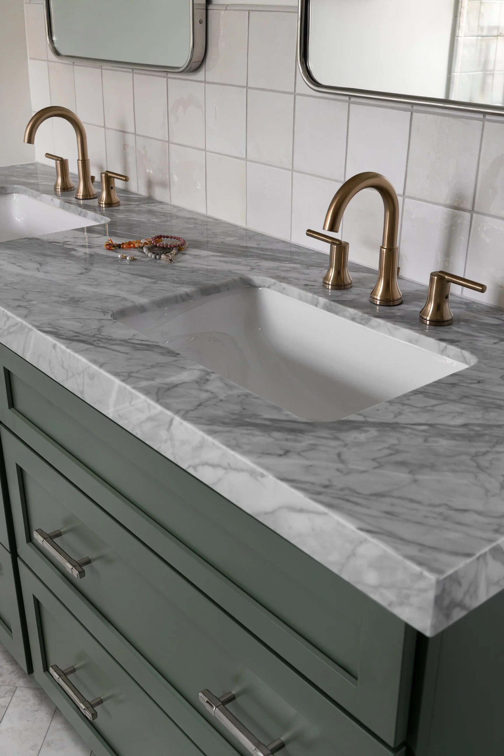 Double vanity with brass accents and dark green coloring for vanity base
