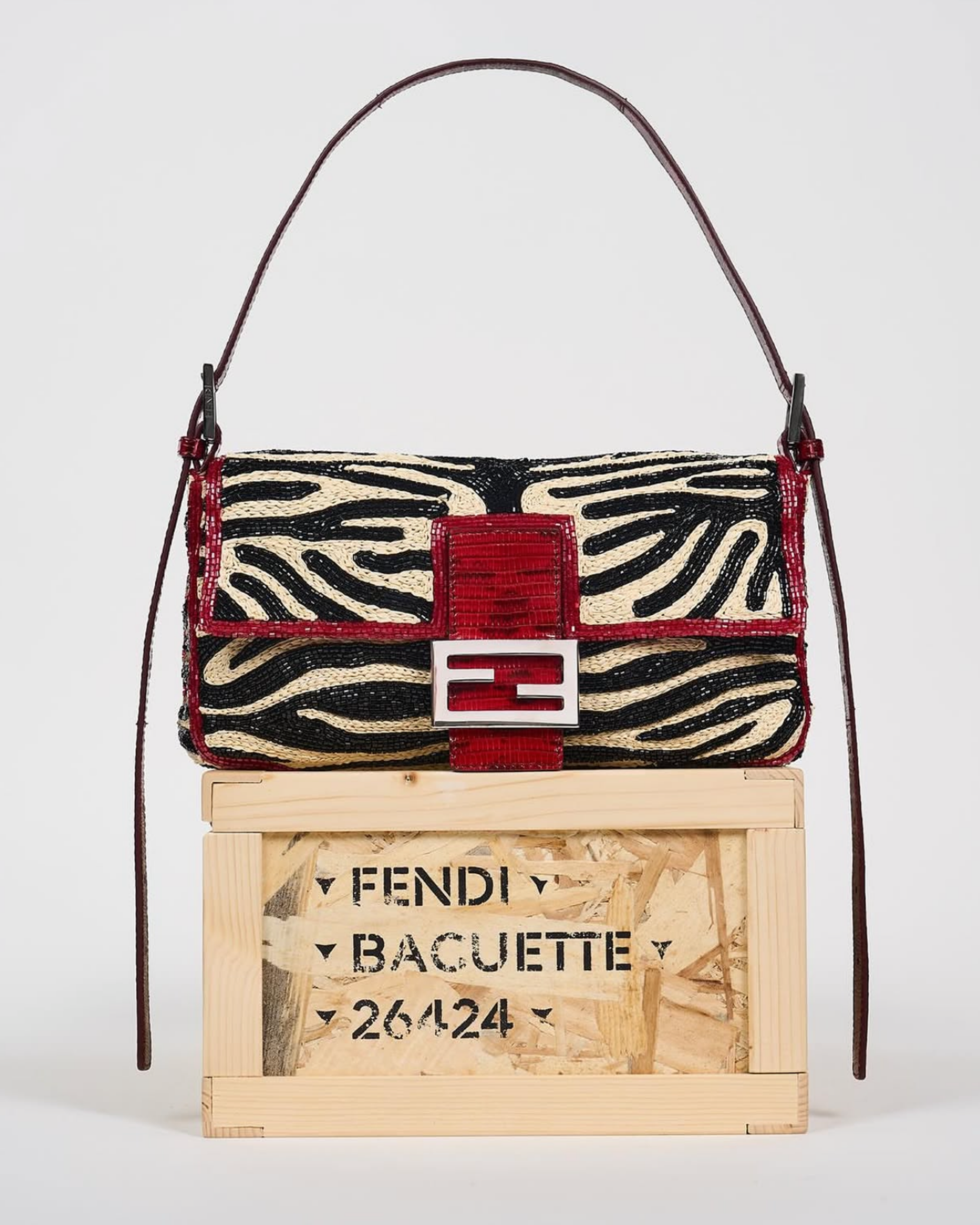 A handbag with a zebra stripe pattern, red accents, and a logo clasp on top, placed on a wooden crate with black text.
