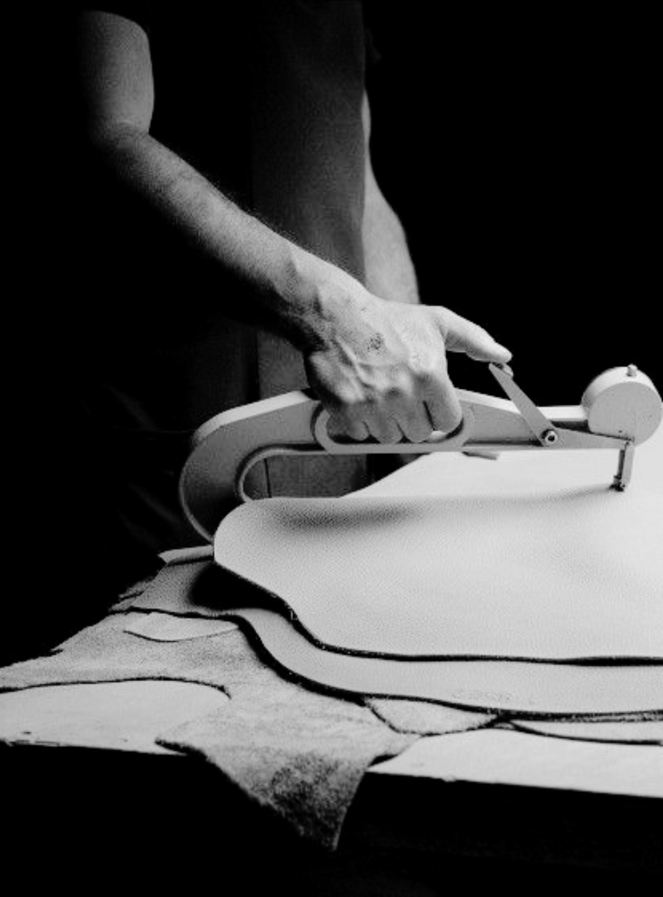 A person using a rotary cutter to cut fabric on a table, with fabric laid out in wavy patterns, in black and white.