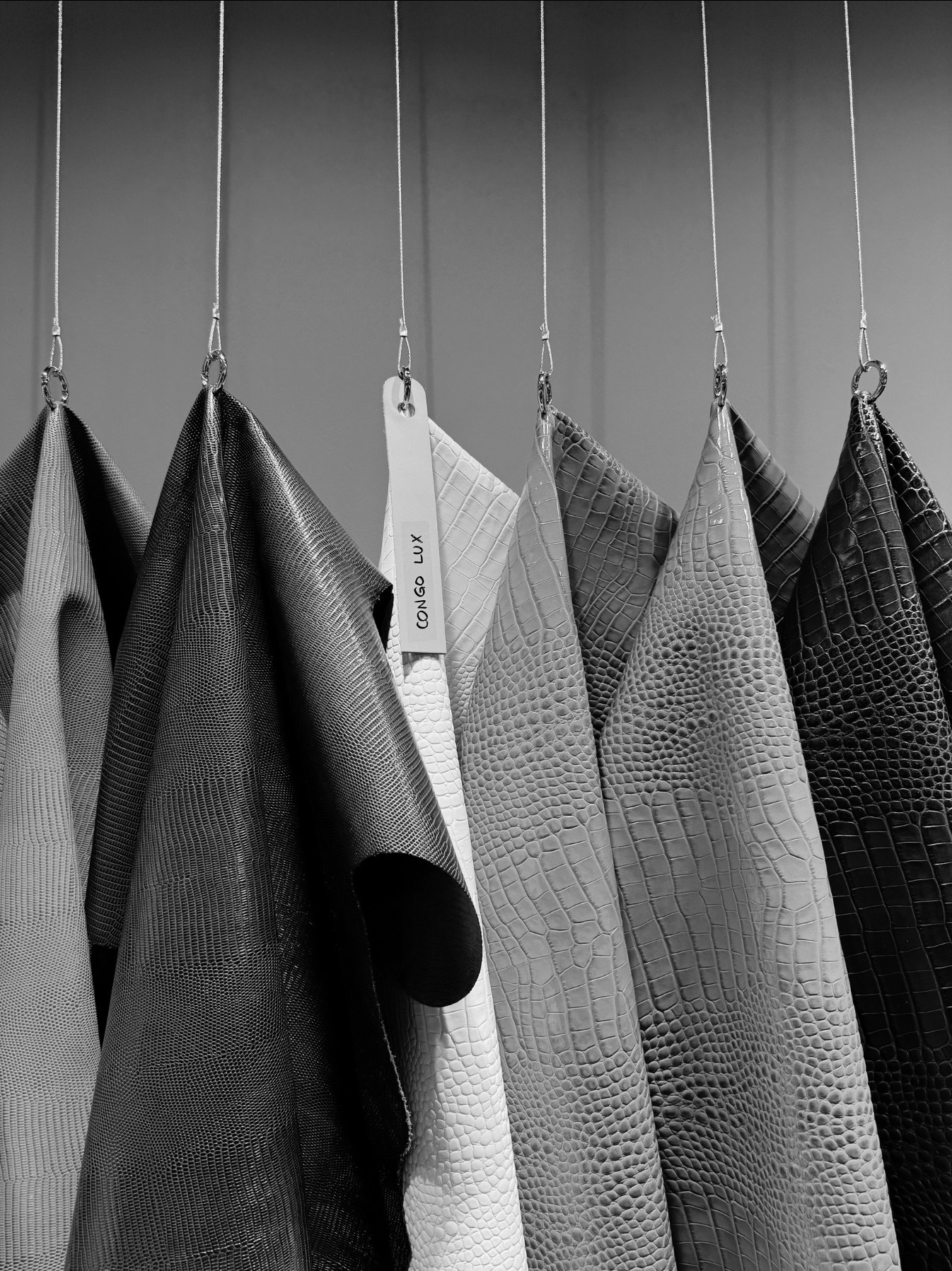 Hanging swatches of textured faux leather or reptile skin-like fabric in shades of black, white, and gray, each with a metal ring and hanging string.