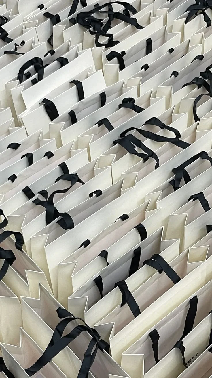 Multiple white shopping bags with black handles arranged in rows.