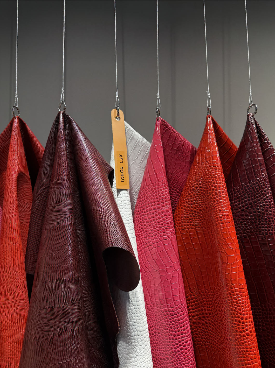 A display of colorful textured leather samples hanging on hooks, including red, maroon, white, pink, orange, and burgundy options.