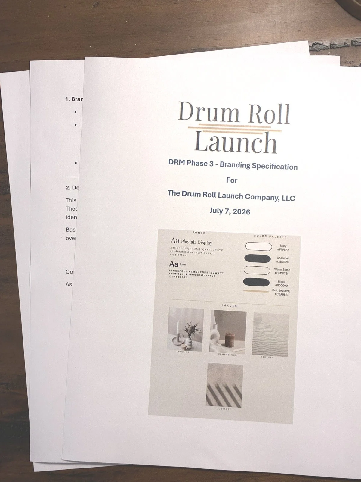 A set of documents, including a branding specification for 'Drum Roll Launch' with details about fonts, color palette, and images, laid out on a wooden surface.