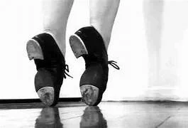 Ballet shoes on a dancer's feet, showing the soles, in a studio or dance floor setting.