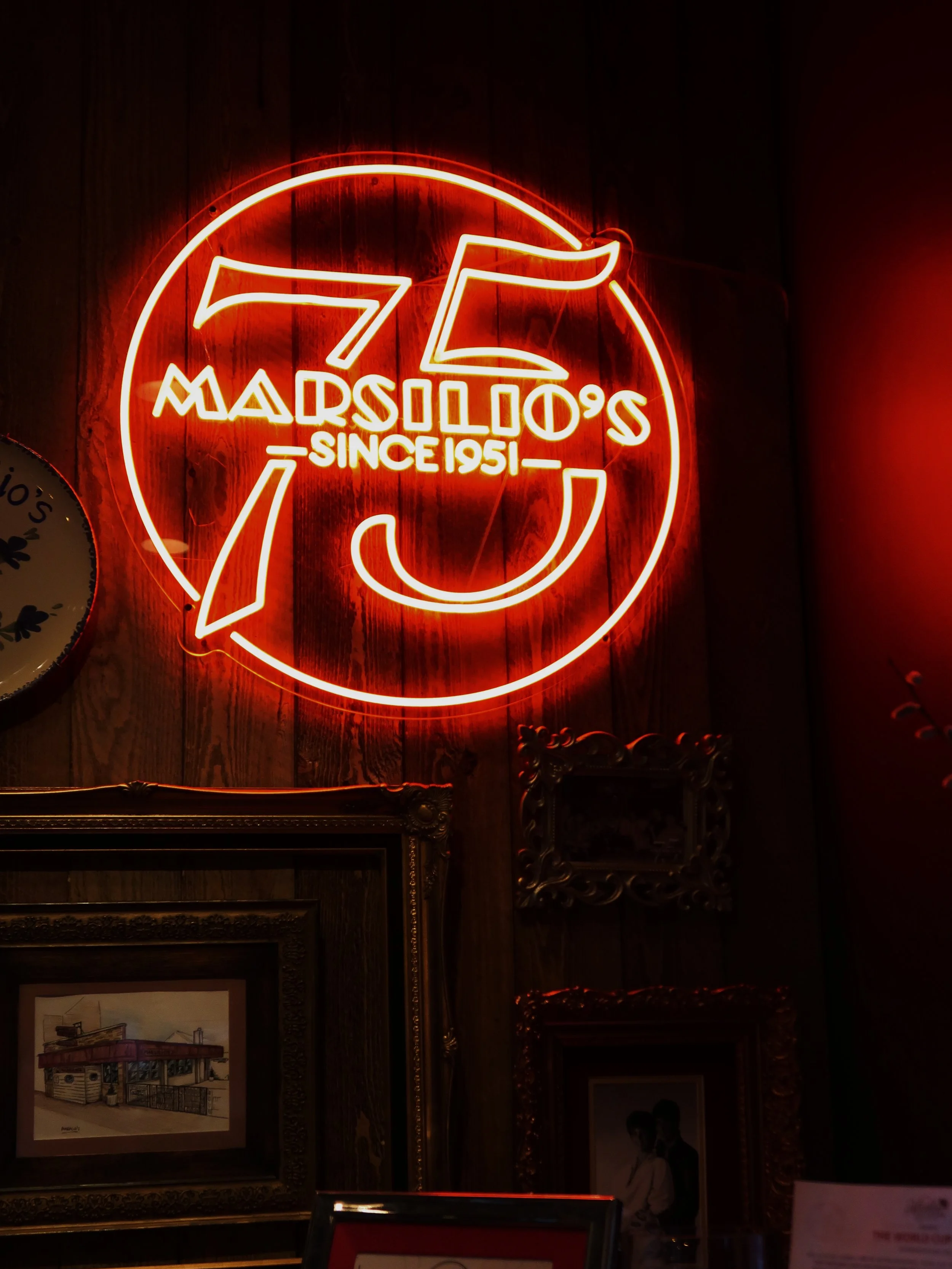 Neon sign displaying the number 76 with the text "Madison's Since 1951" inside a circle, against a wooden wall background.