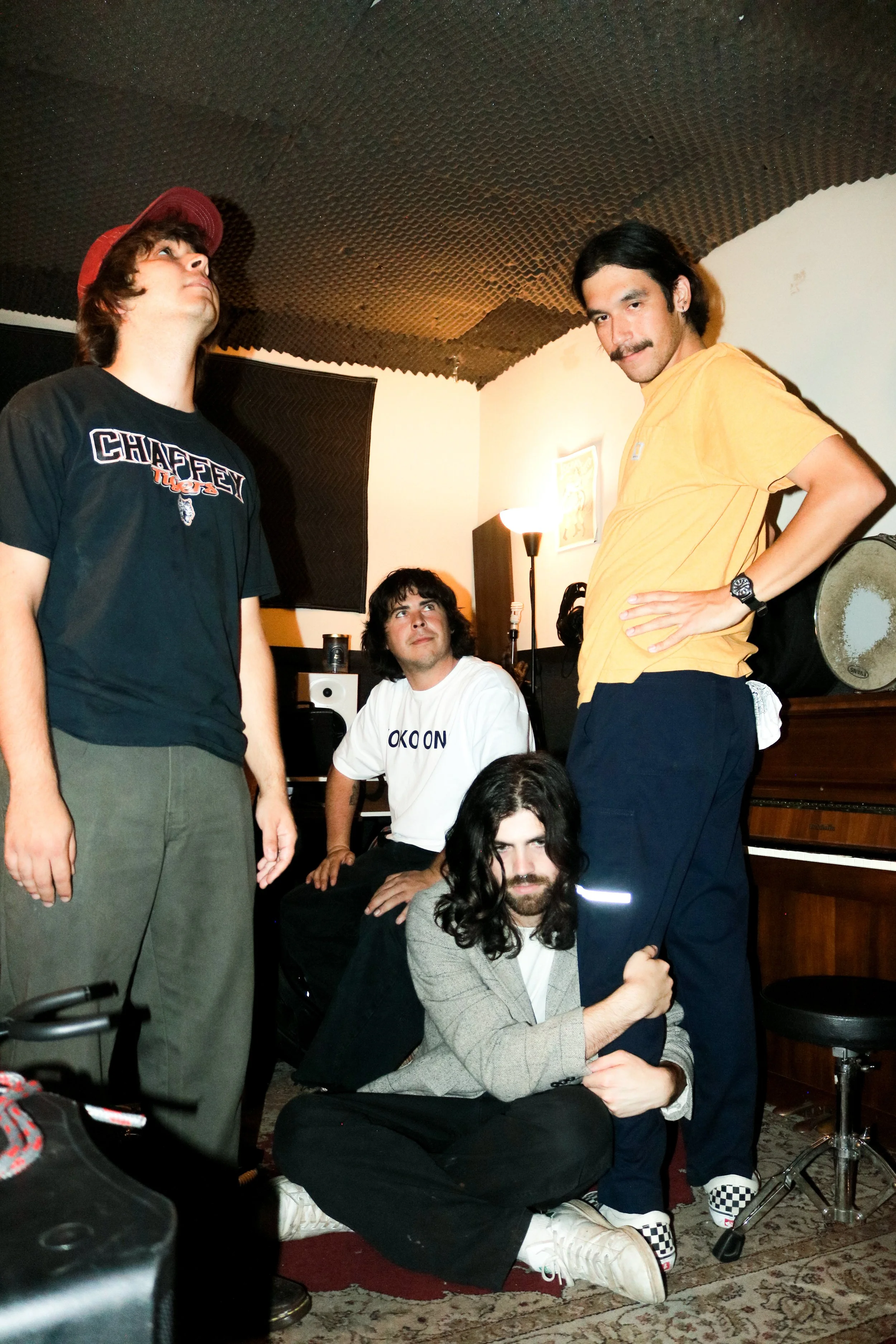 The four members of Los Angeles based rock band M-16 posing in a music studio. Two stand on either side, one sits on the floor clinging to a standing member's leg. Frontman Kyler Hutchison sits in the back gazing upward.