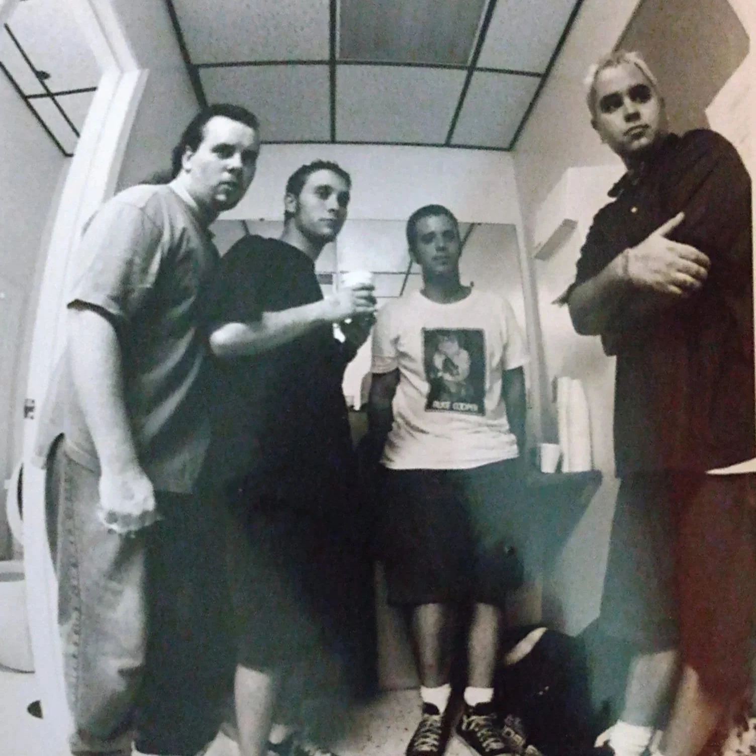 Black and white fisheye lens photo of the St. Louis noise rock band Fragile Porcelain Mice posing for a picture in a small room. The photo is from the 1990s, and the members are still young and dressed casually.