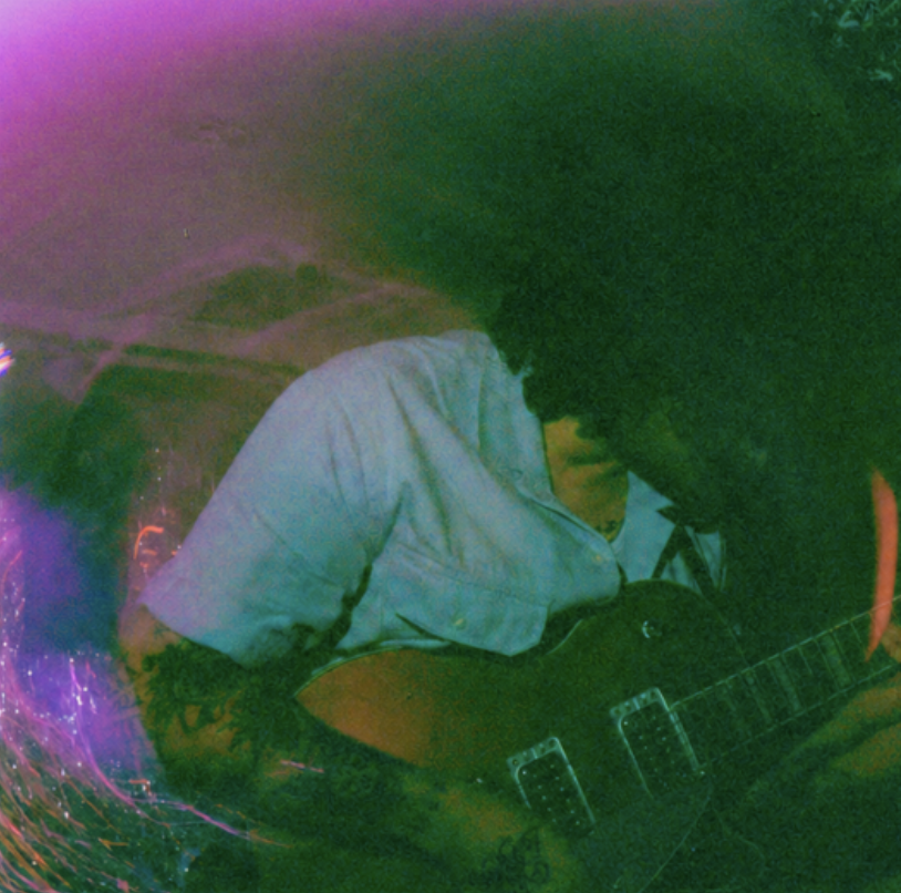 A person playing an electric guitar in a dimly lit room with colorful, abstract lighting.