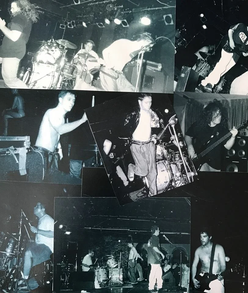 Group of musicians performing on stage, playing various instruments including drums, guitar, and bass, in a dimly lit venue.
