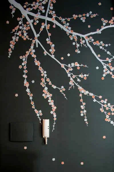 Decorative wall with cherry blossom branch design, a white telephone, and a black object on a dark background.