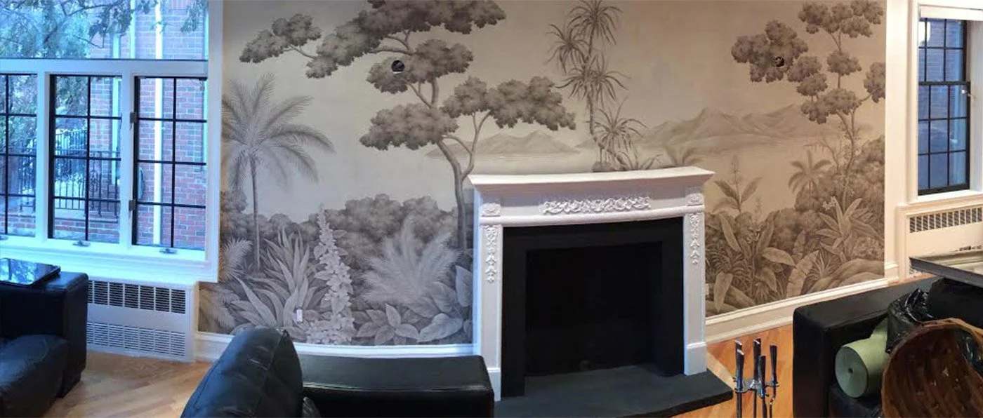 Interior of a living room with a large mural of trees and plants on the wall, a white ornate fireplace, black leather furniture, and windows with black grid frames.