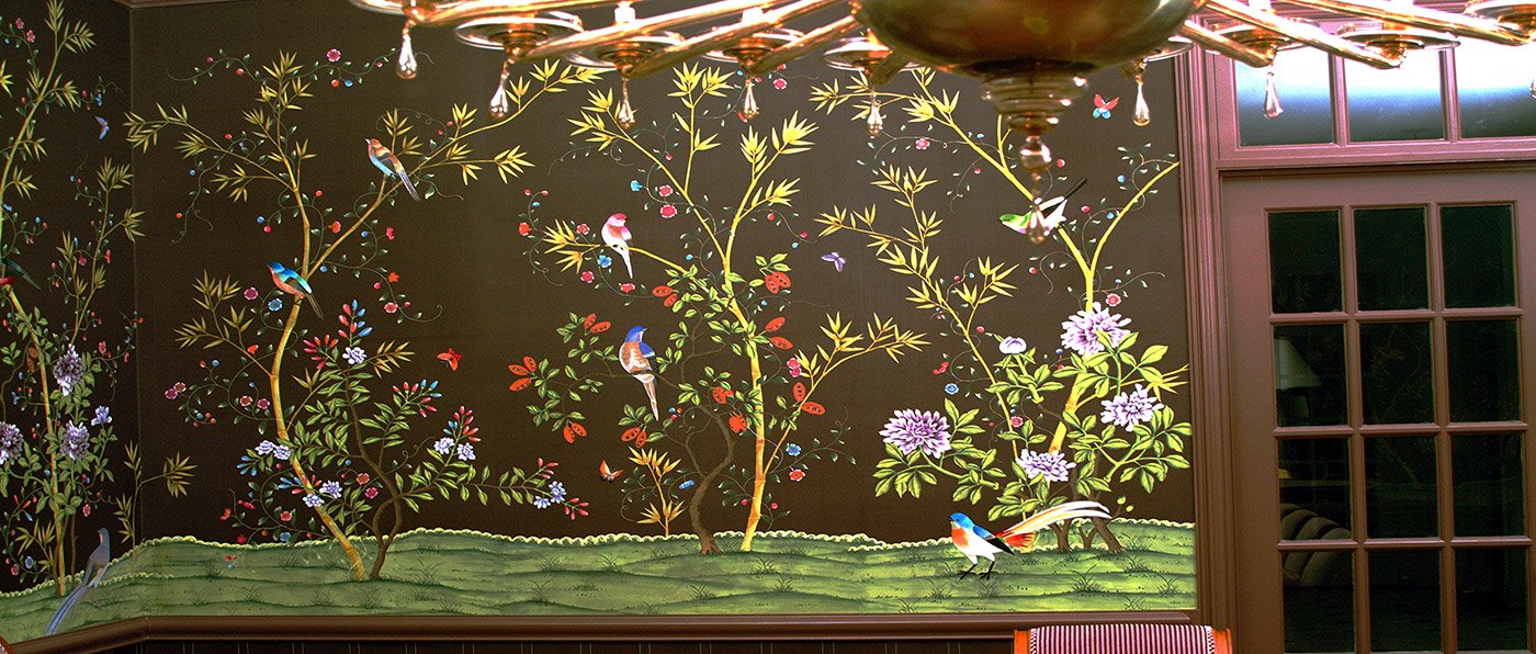 A decorative wall mural featuring painted trees, flowers, birds, and butterflies on a black background in a room with a wooden panel and glass door.