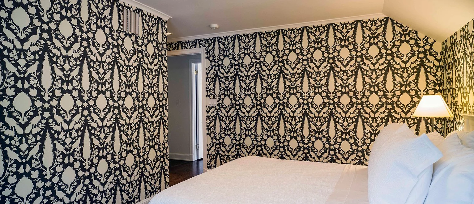 Bedroom with black and white wallpaper, a white bed with white pillows, and a wall-mounted lamp.