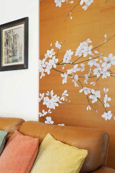 Decorative wall with white floral mural in a living room, with a brown sofa and colorful cushions.