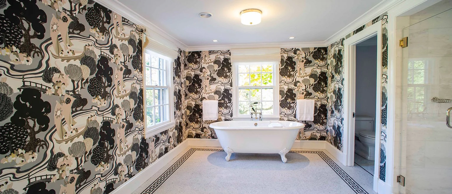 Bright bathroom with black and white patterned wallpaper, a white clawfoot bathtub, and windows allowing natural light.
