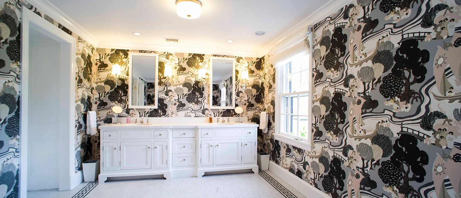A bathroom with papaya-themed wallpaper, two white vanities with mirrors and lamps, a window on the right, and ceiling lights.