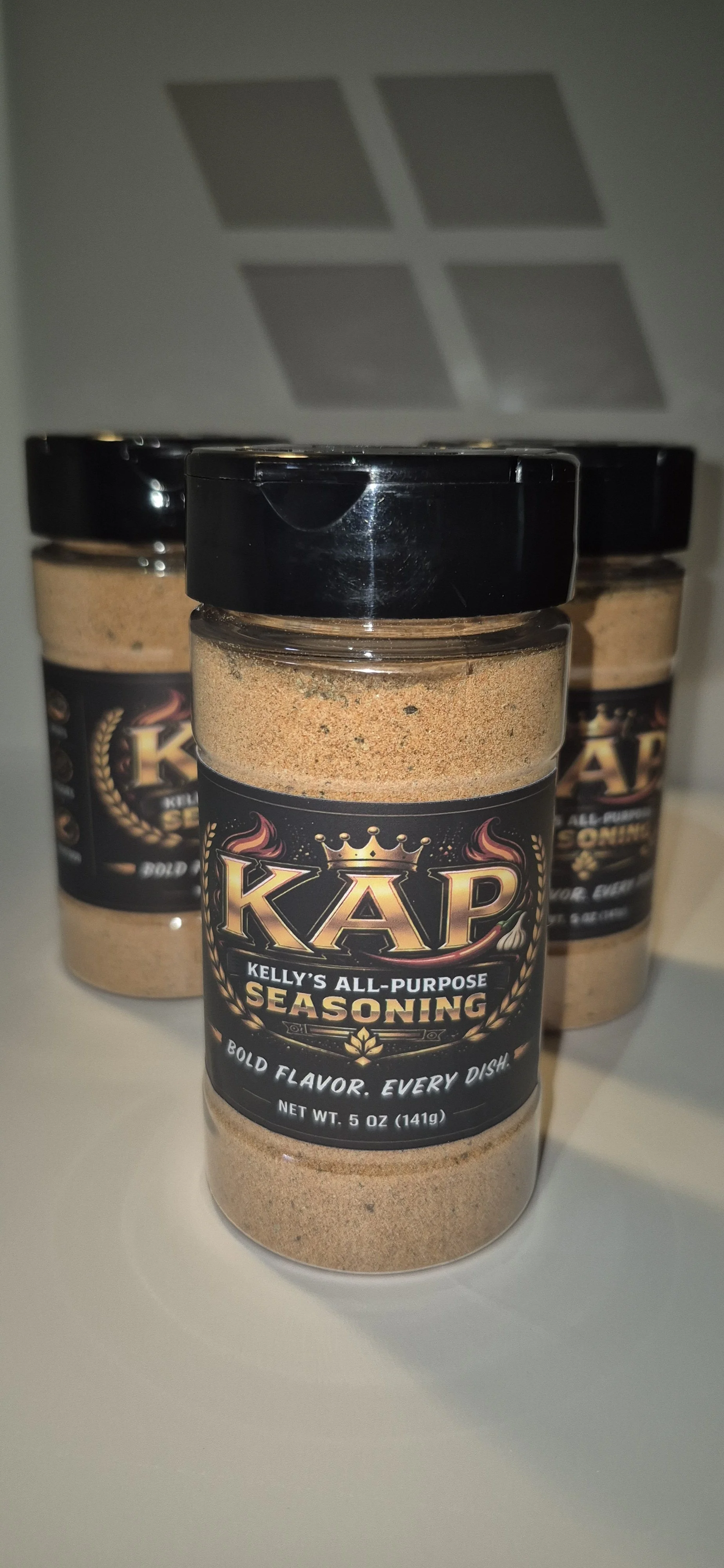 Three jars of Kelly's All-Purpose Seasoning on a white surface with a gray background.