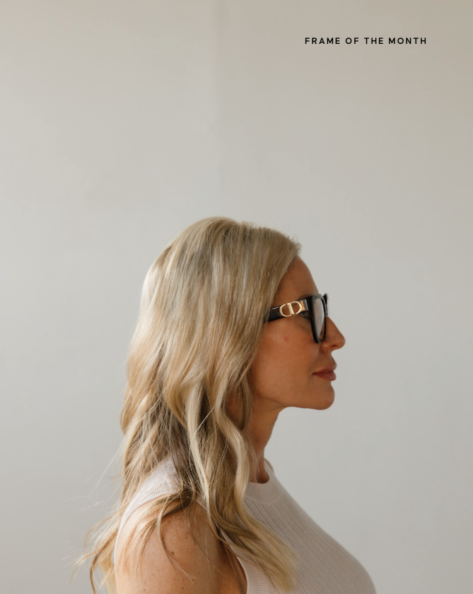 Side profile of a woman with blonde wavy hair wearing black glasses with gold details, against a plain background with text in the top right corner.