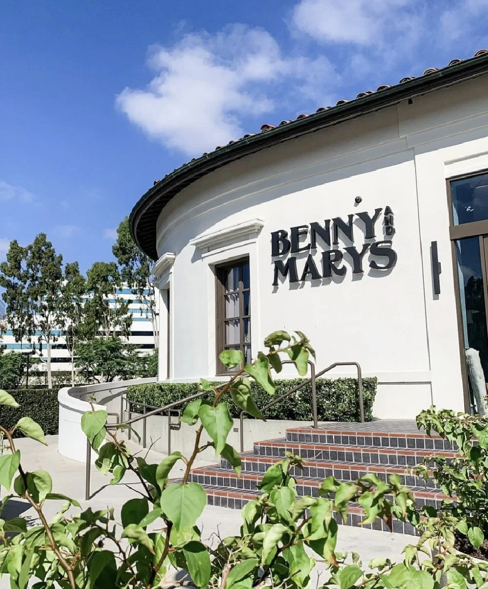 Exterior of a building with a white curved facade, large window, and steps leading up to the entrance, with the sign 'BENNY & MARY'S' on the wall.