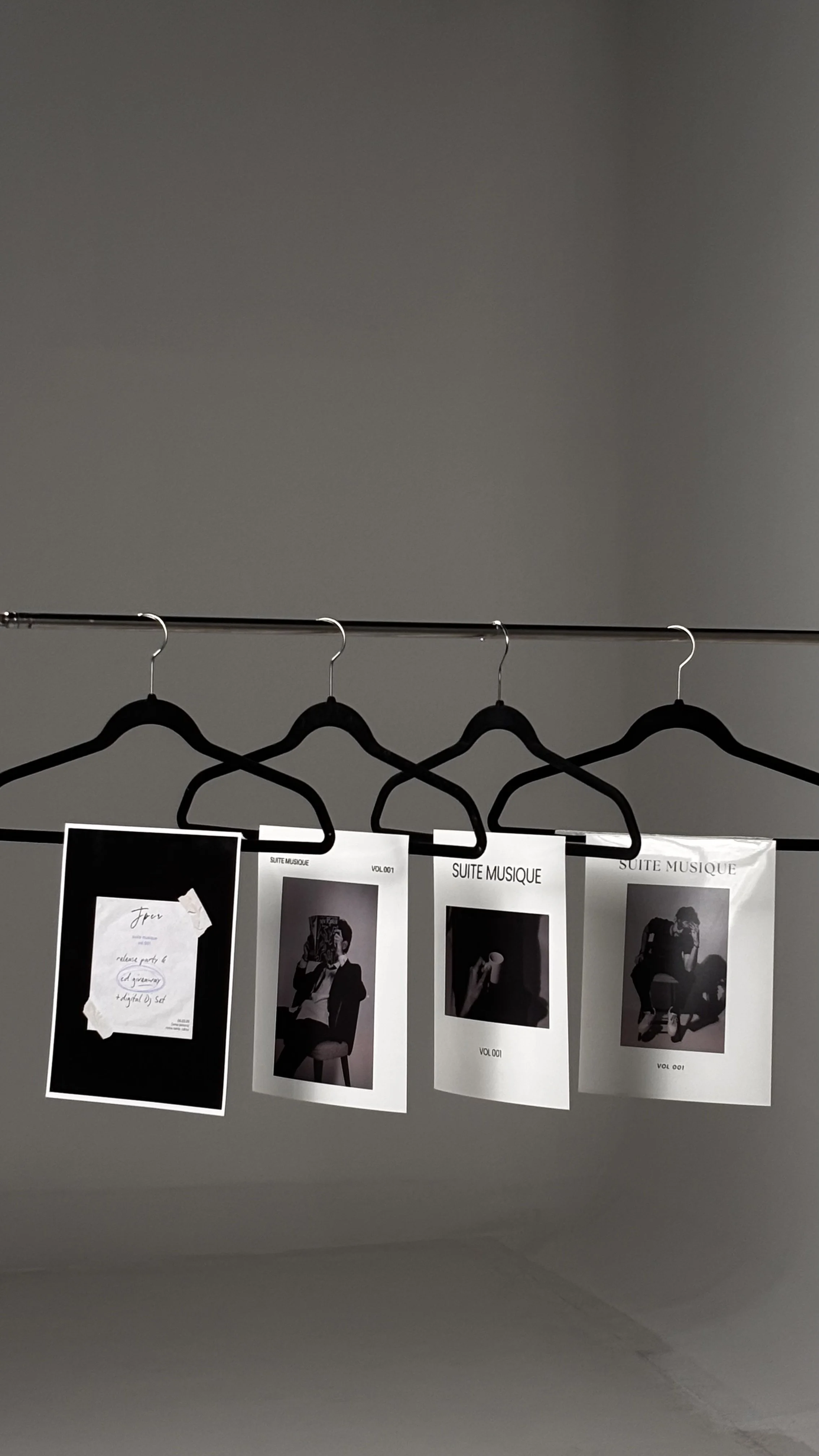 Black hangers hanging on a metal rod with black and white printed paper photos attached, labeled 'SUITE MUSIQUE', against a plain gray background.