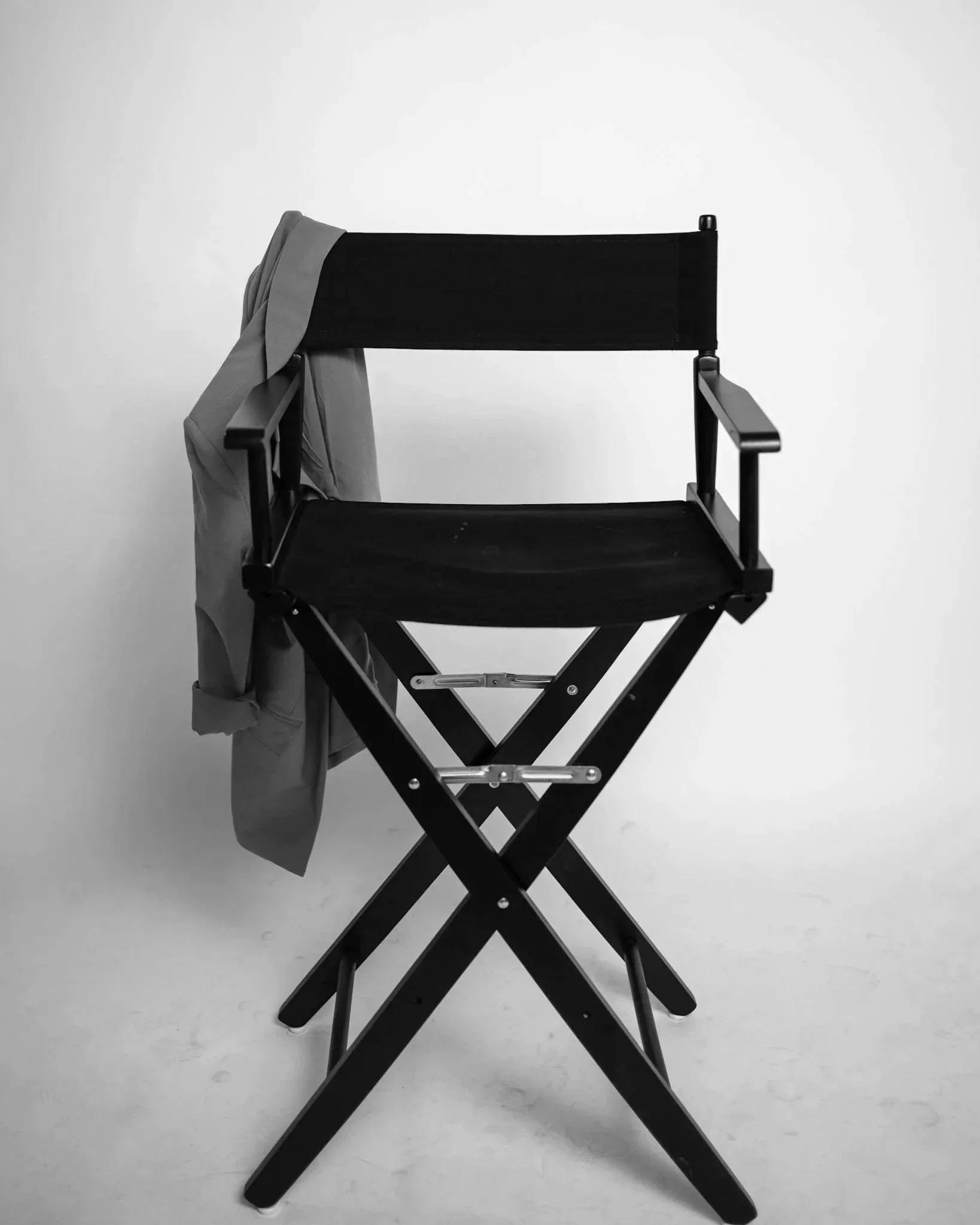 A black director's chair with a light gray jacket draped over one armrest, placed against a plain white background.