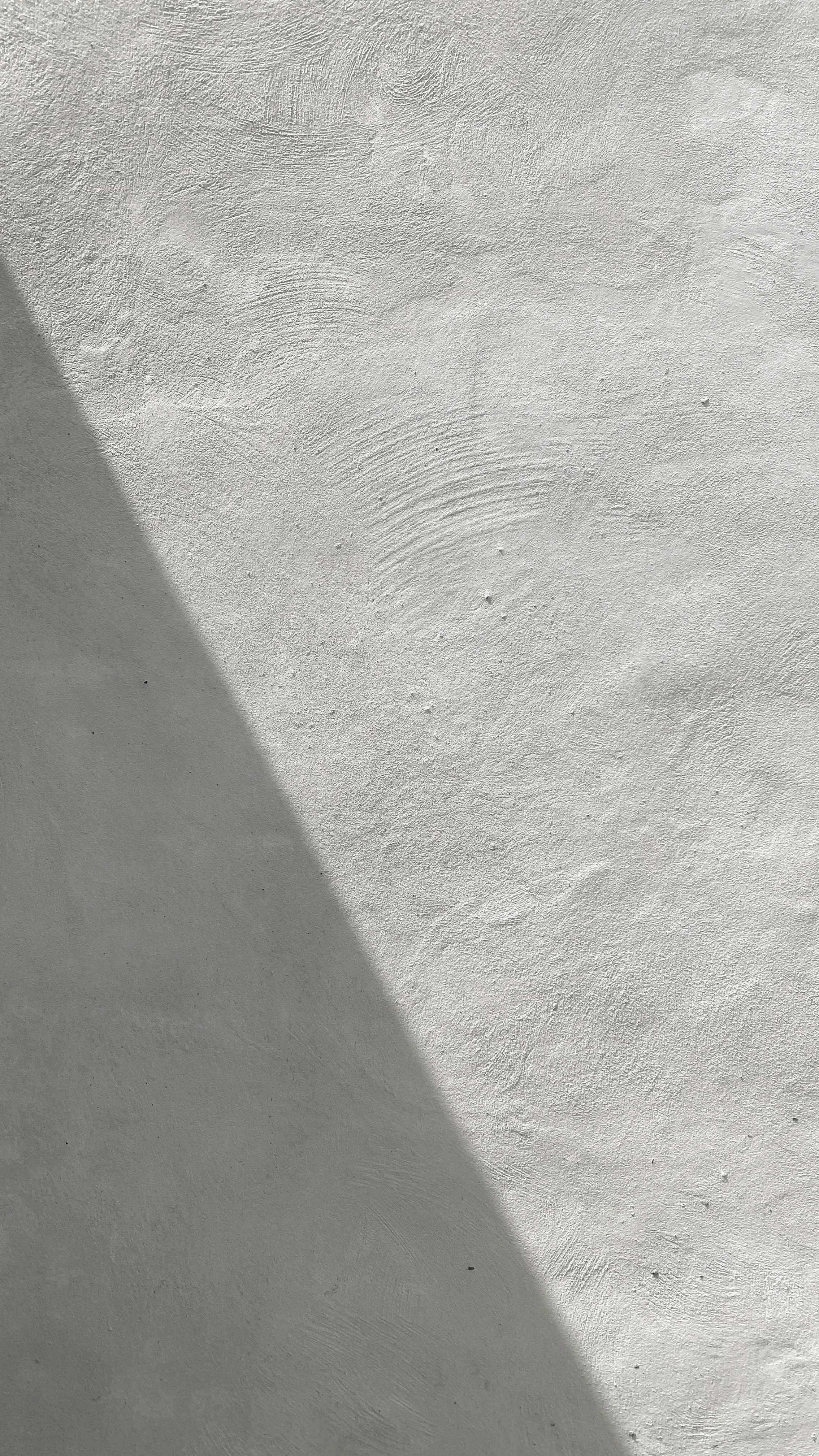 Close-up of a white textured wall with a shadow cast across it.